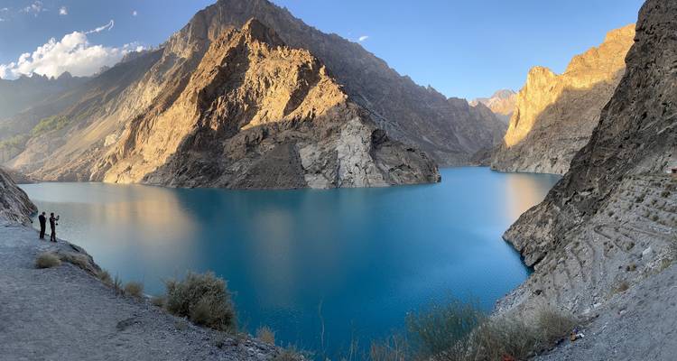 Stunning blue lake with mountainous terrain and two people admiring the view.
