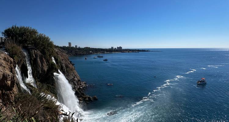 Waterfall flowing into the sea with cityscape in the distance.