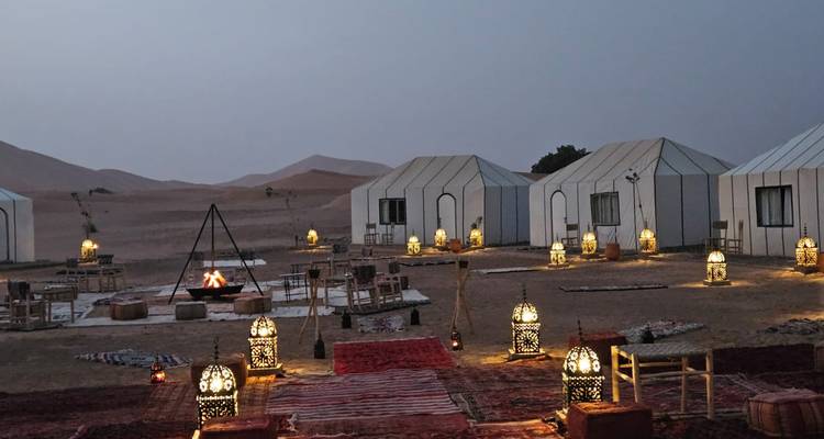 Campement du soir dans le désert avec lanternes allumées et tentes.
