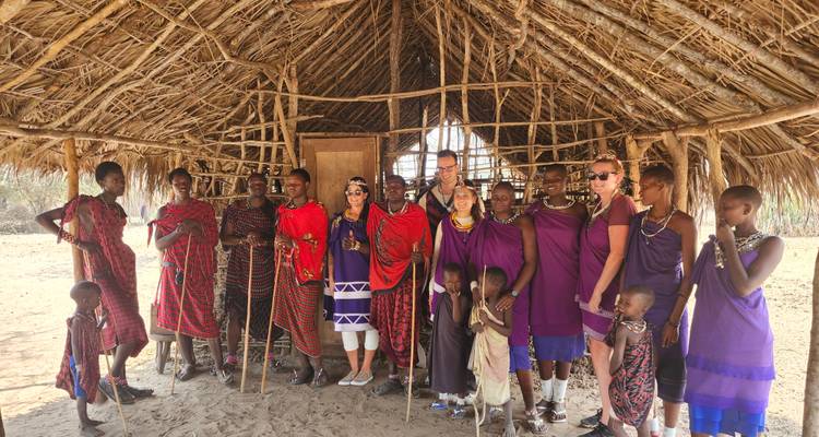 Groupe de personnes en tenue traditionnelle à l'intérieur d'une hutte au toit de chaume.