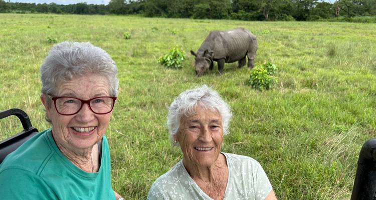 Deux femmes souriantes devant un rhinocéros dans un champ herbeux.