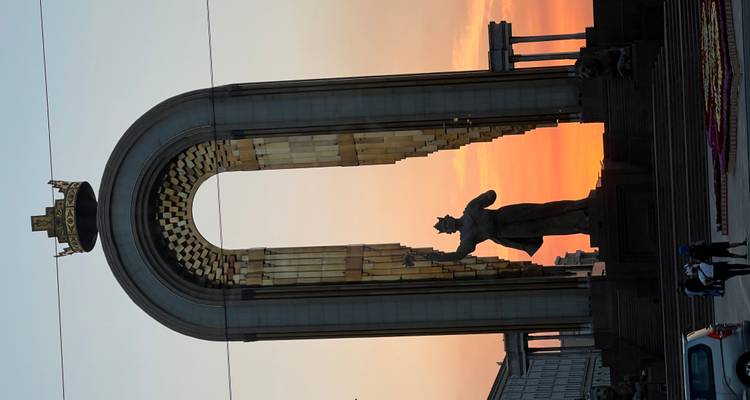 Un grand monument avec une statue et une arche au coucher du soleil.