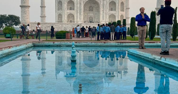 Spiegelung des Taj Mahal im Wasserbecken mit Besuchern im Hintergrund.