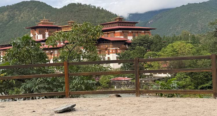 Dzong bhoutanais traditionnel avec des toits rouges et des montagnes vertes.