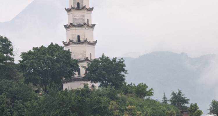 Una torre china tradicional rodeada de árboles con montañas de fondo.