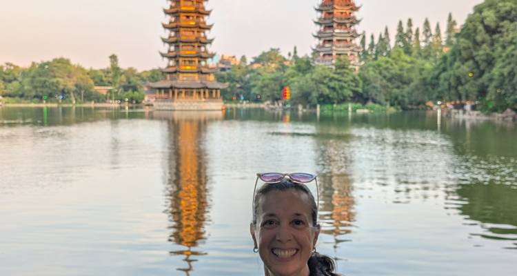Una persona posando junto a un lago con pagodas gemelas al fondo.