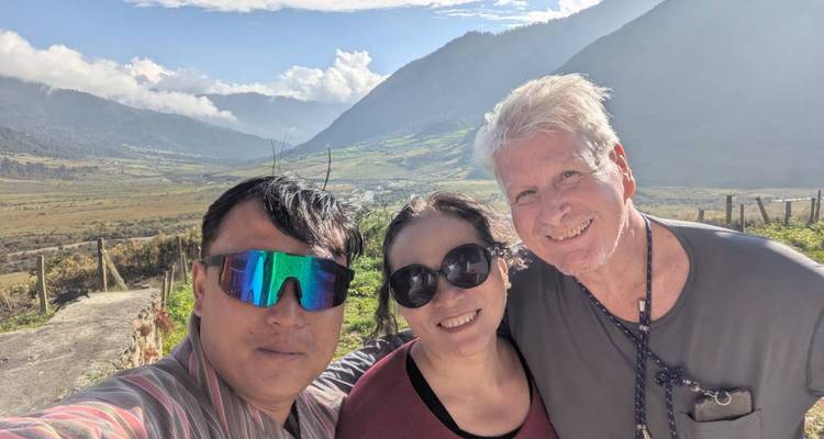 Three people posing with a scenic valley and mountains in the background.