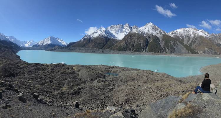 Person sitting by a turquoise lake surrounded by mountains.