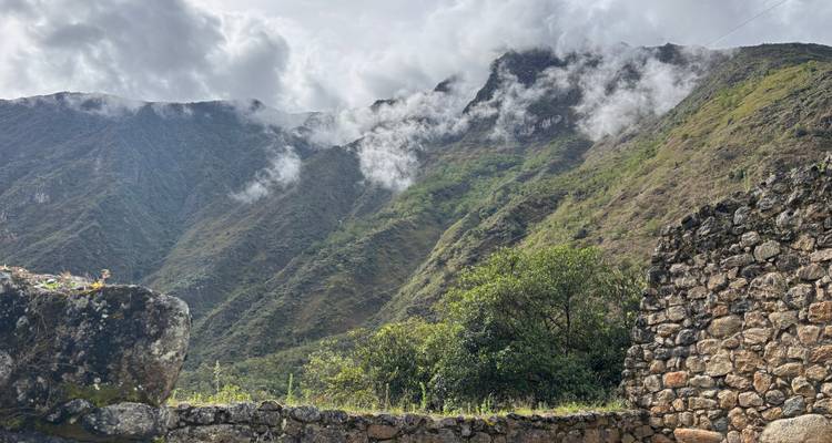 Wolkengeküsste Berge mit alten Steinmauern im Vordergrund.