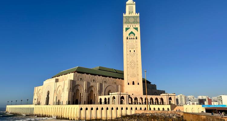Grande mosquée avec un minaret élevé au bord de la mer sous un ciel dégagé.
