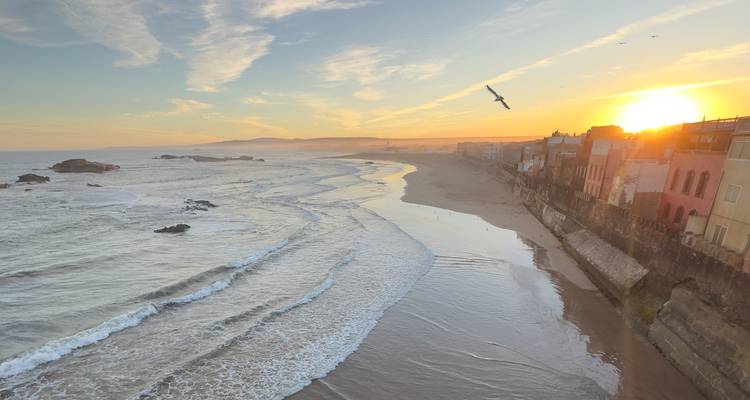 Coucher de soleil sur une plage côtière avec des vagues et un paysage urbain.
