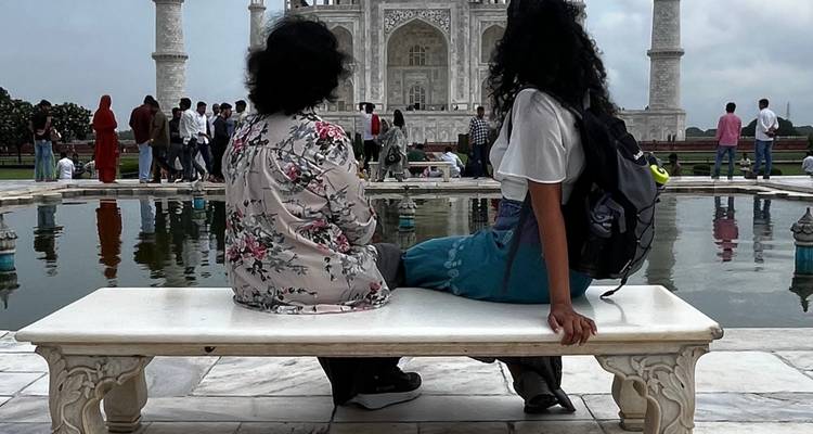 Two people sitting on a bench with the Taj Mahal visible in the background.