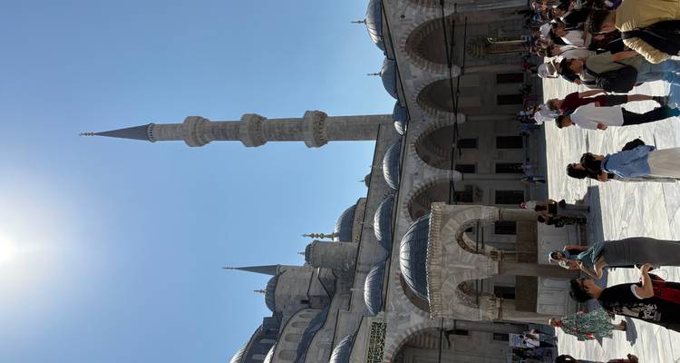 Des personnes visitant la cour d'une mosquée avec un minaret élancé.
