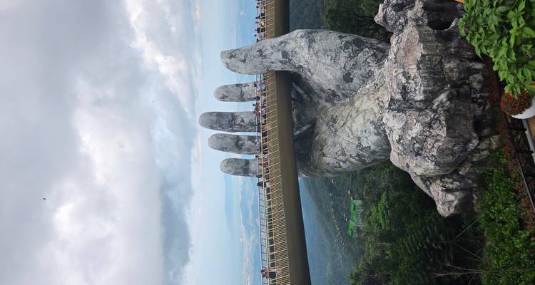 Pont tenu par une main géante de pierre dans un paysage luxuriant.