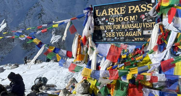 Drapeaux de prière colorés au col de Larke avec un panneau et une montagne enneigée.