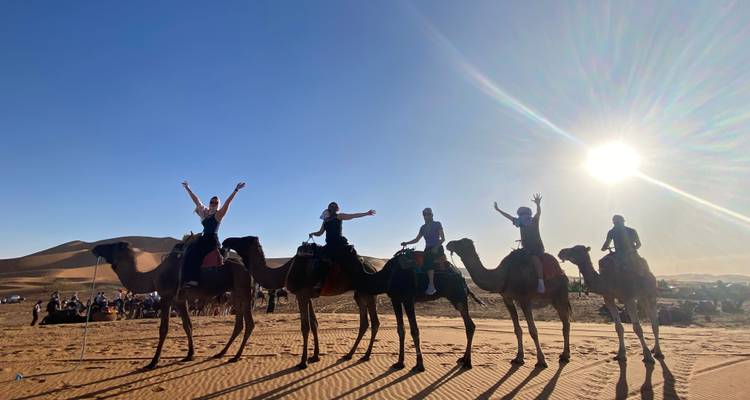 Groupe de personnes montant des chameaux sur une dune de sable.