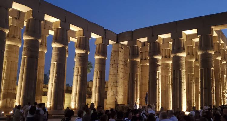Ancient temple columns illuminated at night with people gathered below.