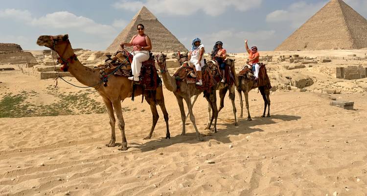 Des gens à dos de chameau avec des pyramides en arrière-plan.