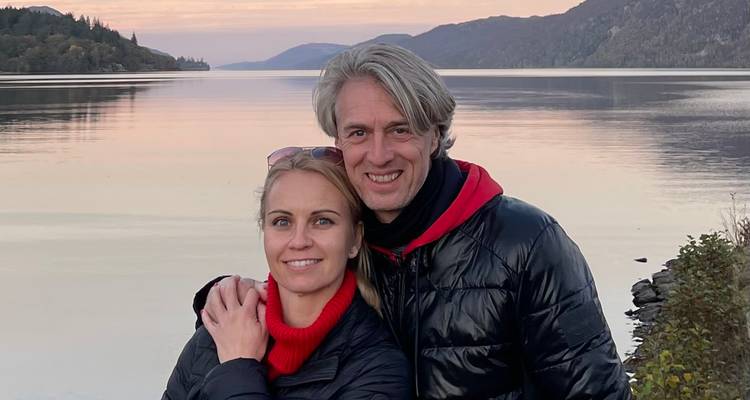 Couple posant près d'un lac calme au coucher du soleil.