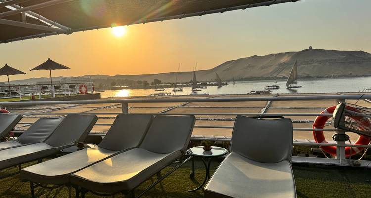 Vue du coucher de soleil depuis le pont d'un navire avec chaises longues and rivière.