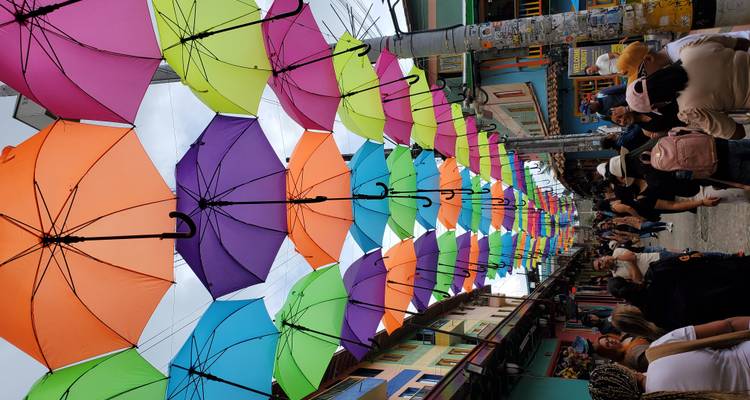 Straat met kleurrijke paraplu's die erboven hangen, druk met mensen.