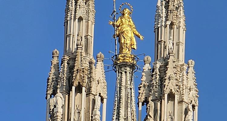 Gouden standbeeld bovenop een gedetailleerde kathedraalspits.