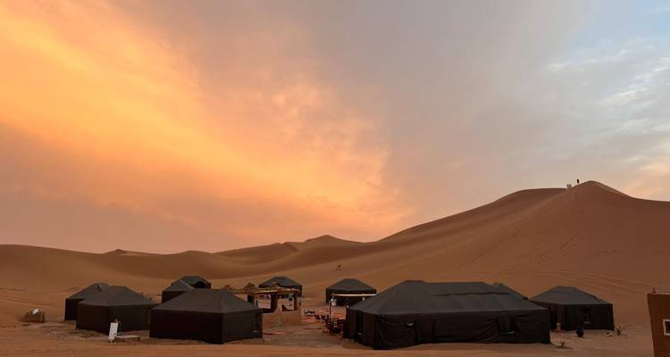 Un campamento en el desierto al atardecer con tiendas de campaña instaladas frente a las dunas de arena.