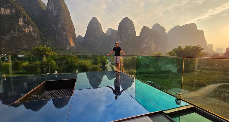 Personne debout sur une plateforme de verre avec un arrière-plan montagneux pittoresque.