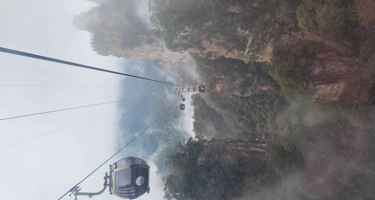 Téléphériques se déplaçant au-dessus d'un paysage montagneux et brumeux.