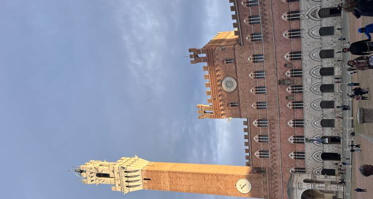Tall brick clock tower in a square with people walking around.