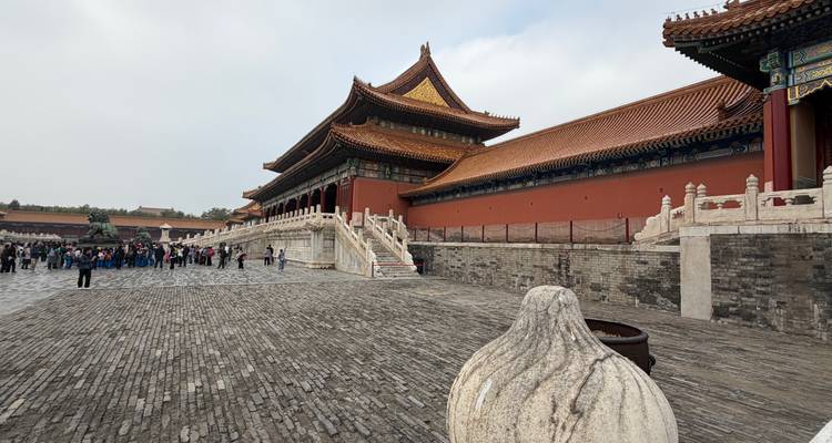 Un vaste complexe historique avec une architecture chinoise traditionnelle et des groupes de personnes sur le pavage de pierre. Les bâtiments ont des toits complexes avec des tuiles dorées et des murs rouges.