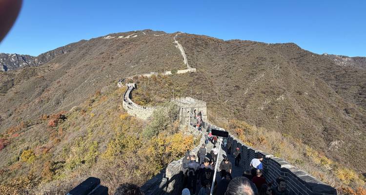 Une section de la Grande Muraille de Chine s'étendant à travers un paysage montagneux sous un ciel bleu dégagé. Des touristes marchent le long de la muraille.