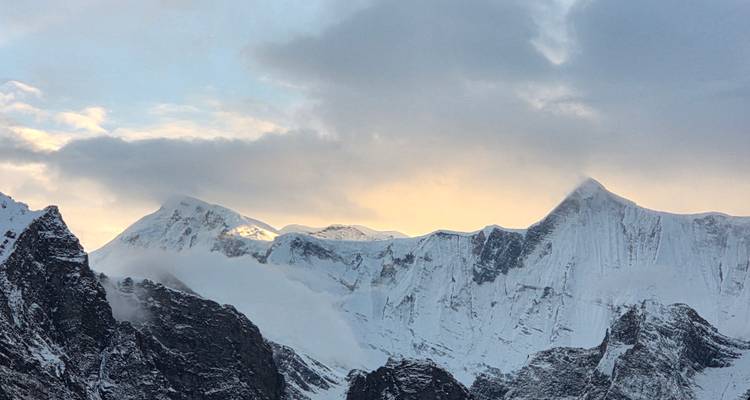Snow-capped mountain range with clouds and sunlight.
