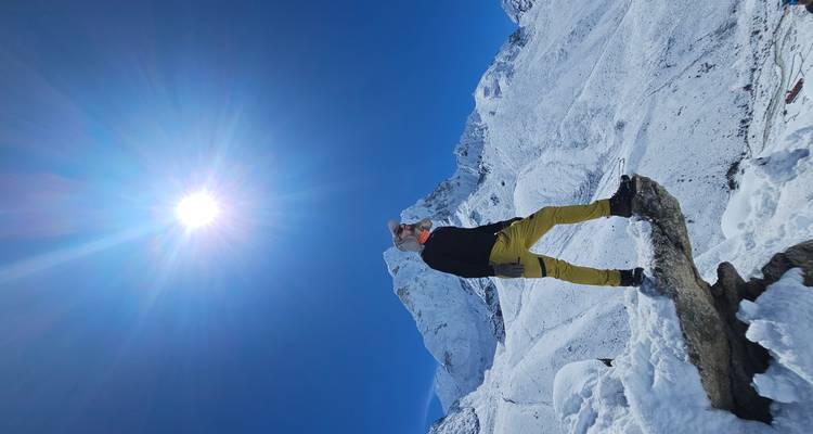 Person standing on a snow-covered rock with a bright sun in the clear sky.