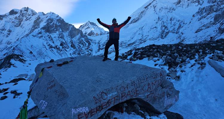 Person triumphantly standing on a boulder with 'Everest Base Camp' written on it.