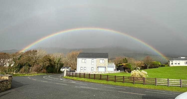 House with a vivid rainbow arching over a cloudy sky
