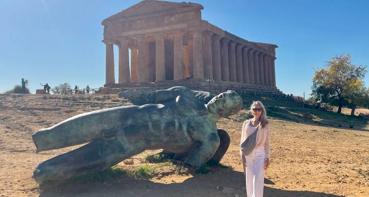 Persoon die poseert voor een historische tempel en omgevallen standbeeld