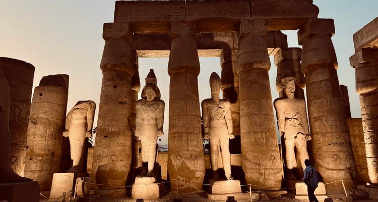 Illuminated statues and columns of an ancient Egyptian temple at dusk.