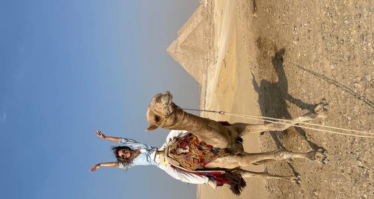 Persoon die op een kameel rijdt met piramide op de achtergrond.