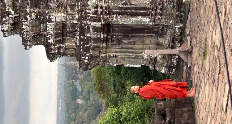 Monnik die een historisch stenen bouwwerk observeert met bomen op de achtergrond.