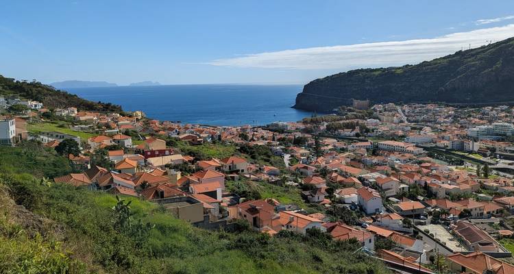 Une vue panoramique d'une ville côtière avec des bâtiments aux toits rouges et la mer.