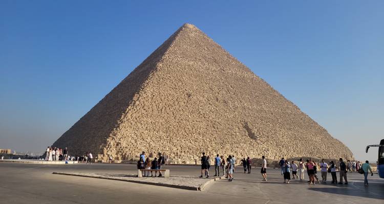 Die Große Pyramide von Gizeh mit Touristen, die bei klarem Himmel um sie herumgehen.