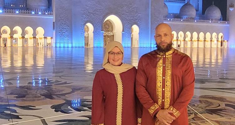 Zwei Menschen in traditioneller Kleidung vor einer kunstvoll beleuchteten Moschee bei Nacht.