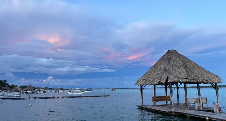 Eine ruhige Lagune mit einem strohgedeckten Steg bei Sonnenuntergang.