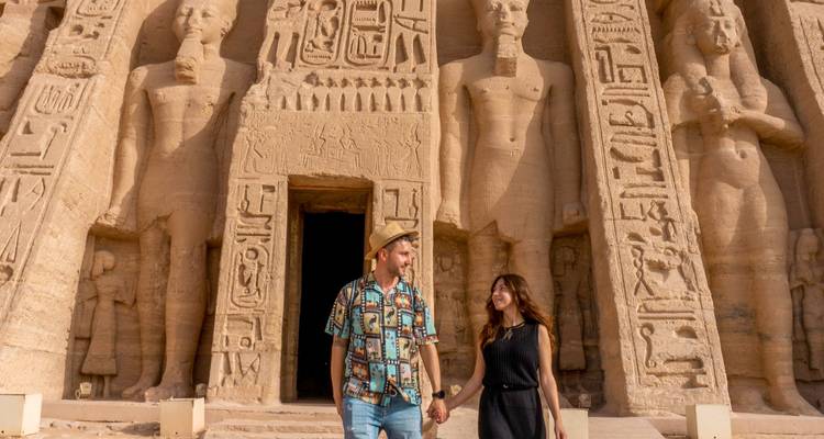 Una pareja tomada de las manos frente a estatuas antiguas egipcias talladas.