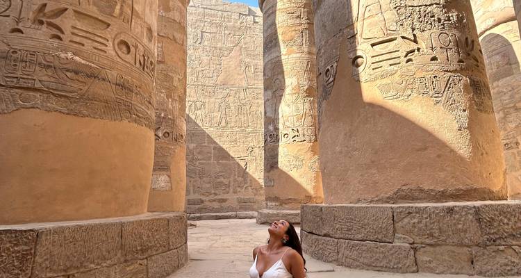 Eine Frau, die zu großen altägyptischen Säulen mit Hieroglyphen aufblickt.