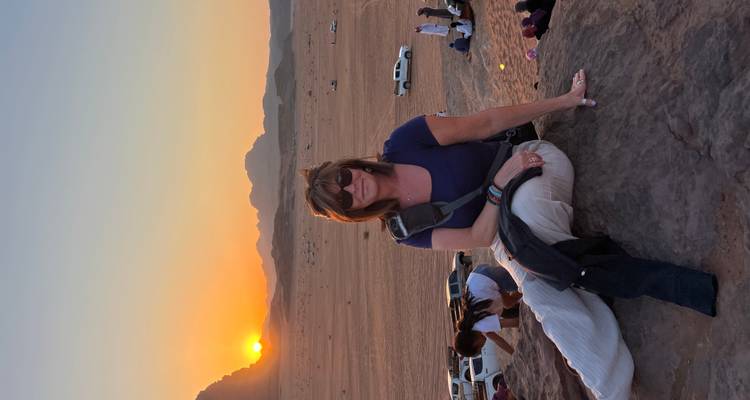 Person auf Felsen sitzend mit Wüstenlandschaft und Sonnenuntergang.