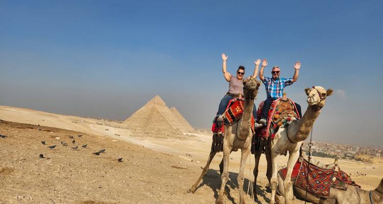 Personas montando camellos frente a las pirámides.