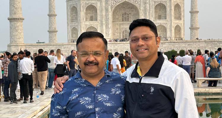 Twee mannen glimlachend voor de Taj Mahal met een menigte.