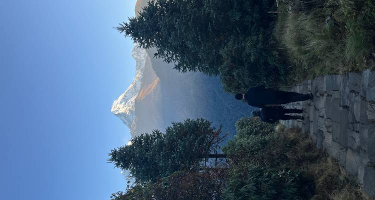 Twee mensen wandelen op een bergpad met een besneeuwde bergtop op de achtergrond.
